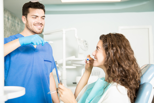 Image of a dental professional showing a patient how to brush her teeth, at Martin Periodontics in Mason, OH.