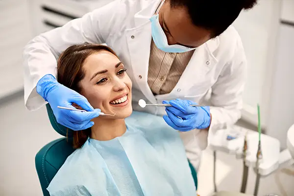 A smiling female patient undergoing a dental exam performed by a dentist wearing blue gloves in a clean, modern clinic.